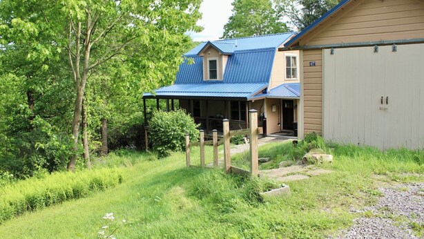 A two-story house with a blue roof, a porch, and a garage. - Charming 1920s Hillside Home Overlooking Valley and Rails-To-Trails (Rimersburg)