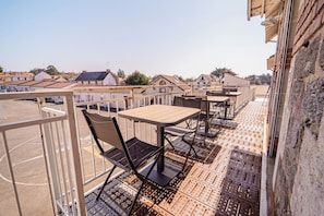 A rooftop terrace with tables and chairs, a view of surrounding buildings, and a brick wall.