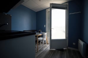 A room with a kitchen area, a dining table with chairs, and a large window with blinds.