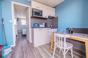 A compact kitchen with a microwave, kettle, and coffee maker. A small dining table with chairs is in the foreground.