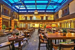 A spacious indoor dining area with multiple tables and chairs, a high ceiling with a glass roof, and traditional decor. - Shangri-La 5th Asterly Stone Tiankui Hotel (Dukezong Ancient City Shop) (Shangri-La)
