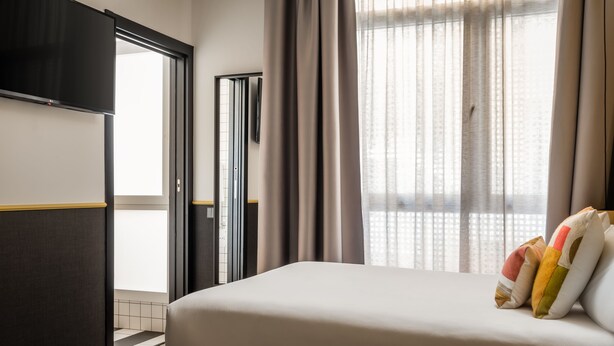 Habitación de hotel con cama, televisión, armario y ventana con cortinas.