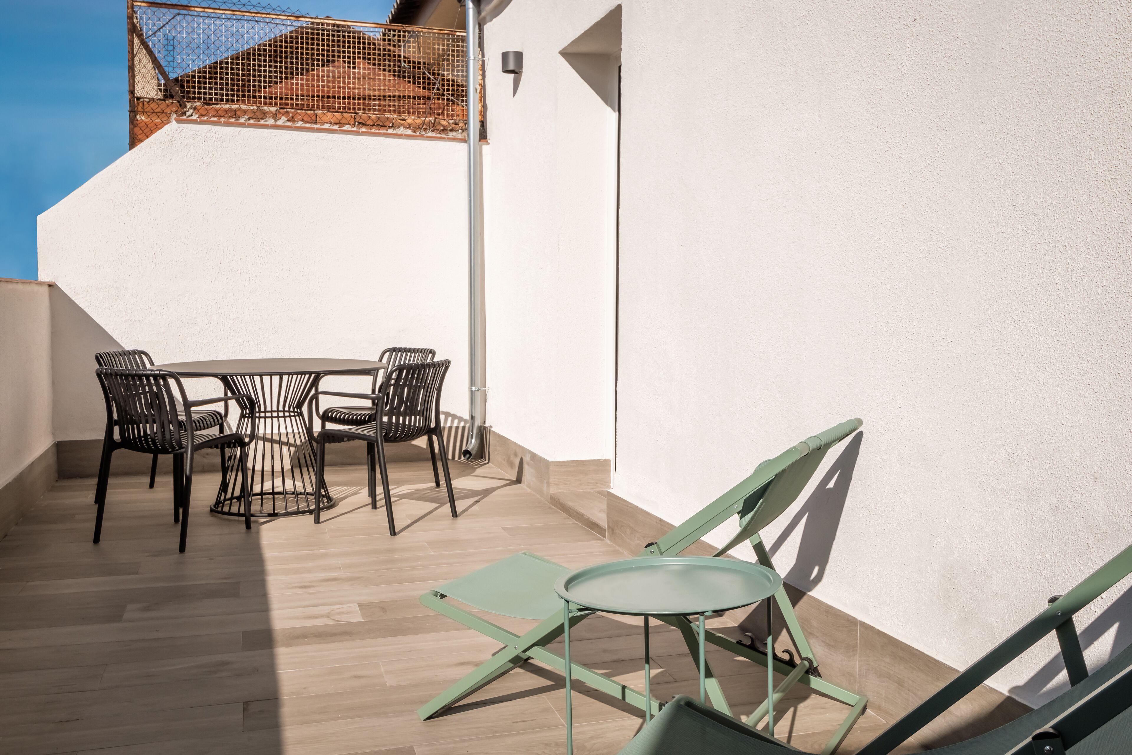 Un balcón con una mesa y sillas, una silla de metal y una silla plegable verde.