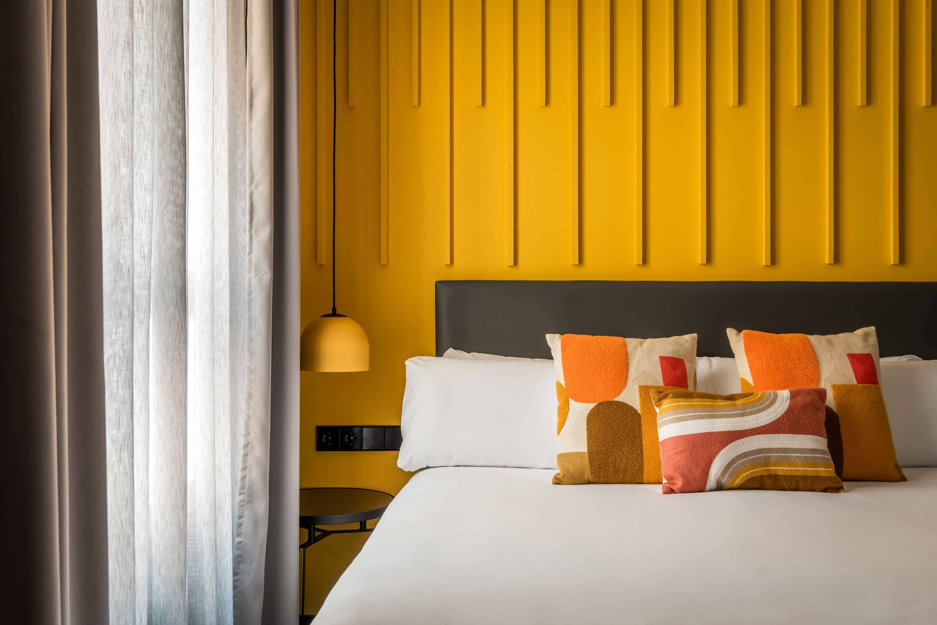 Una habitación de hotel con cama, almohadas, mesita de noche y lámpara.