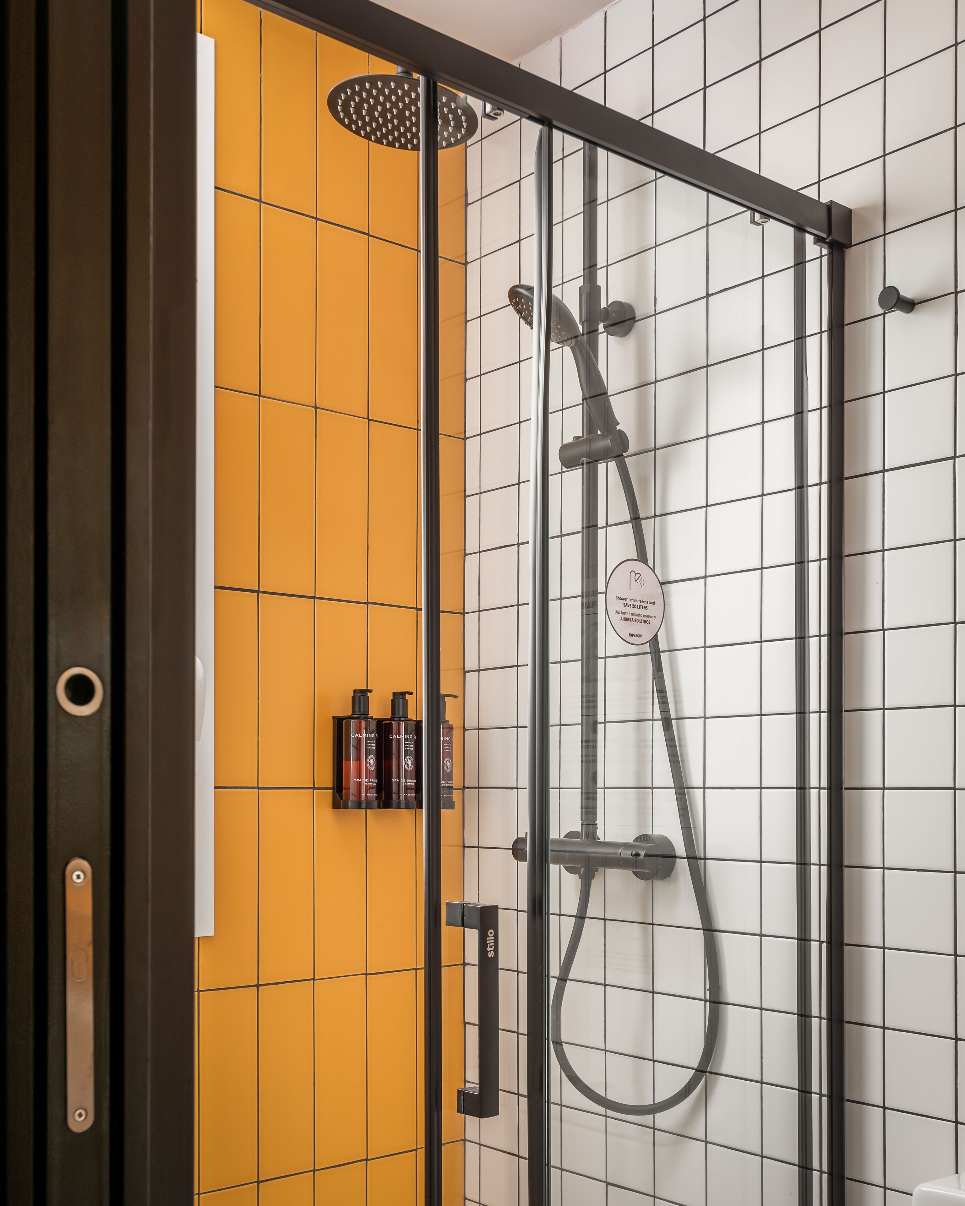 A modern shower enclosure with a glass door, a yellow tiled wall, and a black frame.