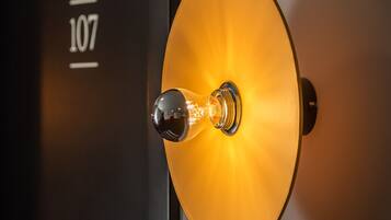 A close-up of a wall-mounted light fixture with a clear glass cover and a metallic base, set against a dark background with a number "107" visible.