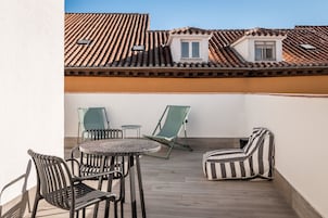 A terrace with a round table and chairs, a striped sofa, and a small window.