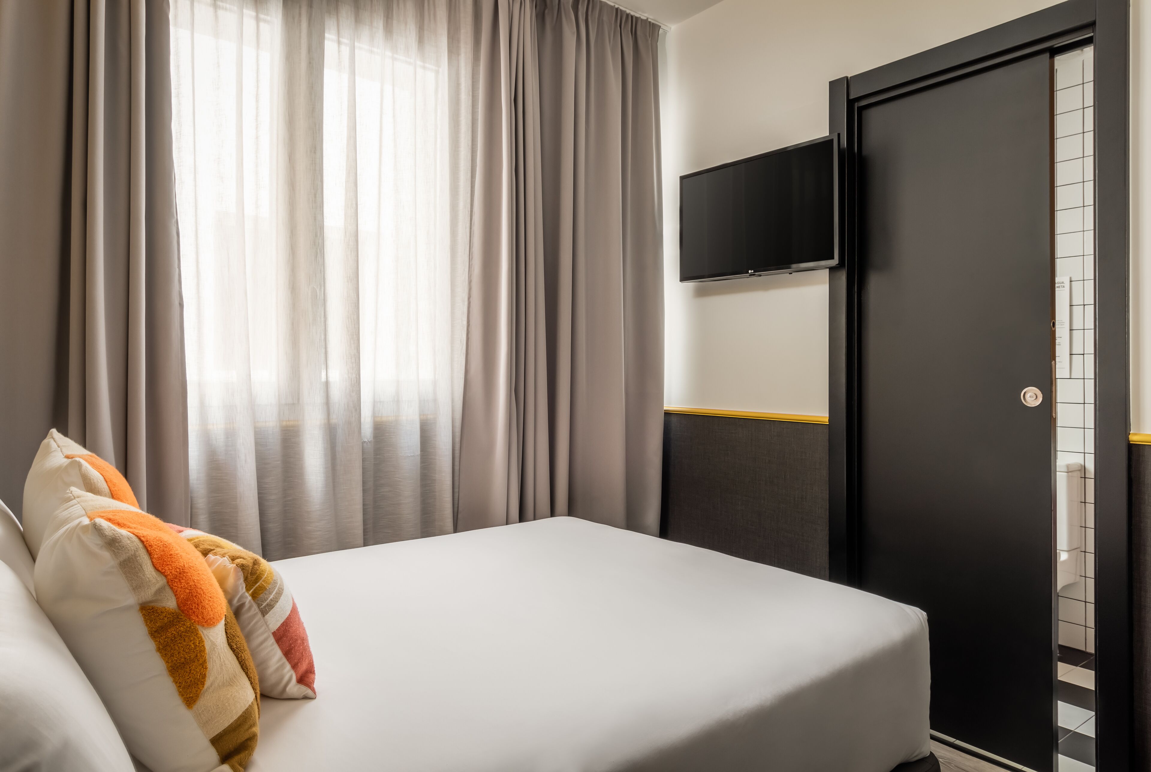 A hotel room with a bed, curtains, a television, and a wardrobe.