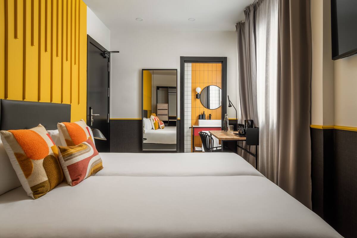 Quarto de hotel com uma cama grande, uma escrivaninha com cadeira, um espelho e uma televisão.