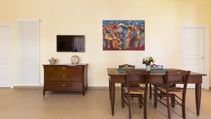 A dining area with a wooden table and chairs, a television mounted on the wall, and a painting above the table. - Court of Nobles (Conversano)