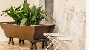 A wooden planter with green plants, a white metal table, and two white metal chairs against a stone wall. - Court of Nobles (Conversano)