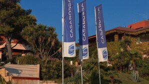 Tre flag med teksten "CASAROSA" og "Future", en bygning med rødt tag og vegetation.