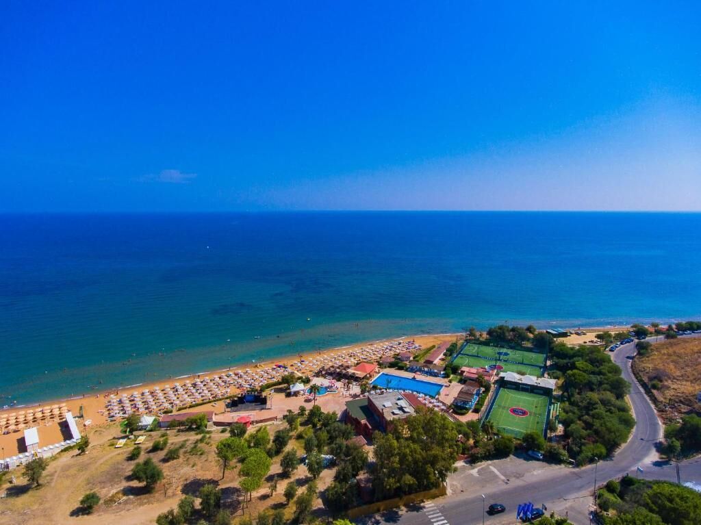 Vue aérienne d’une zone côtière comprenant une plage, un complexe sportif et une route.