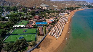 Oversigtsbillede af et kystresort med en lang sandstrand, en swimmingpool og en tennisbane.