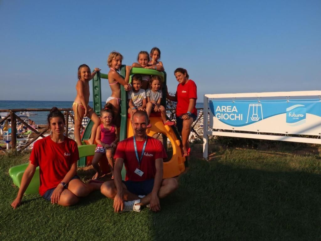 A group of people posing in front of a banner with the text "AREA GIOCHI" and "Futuro".