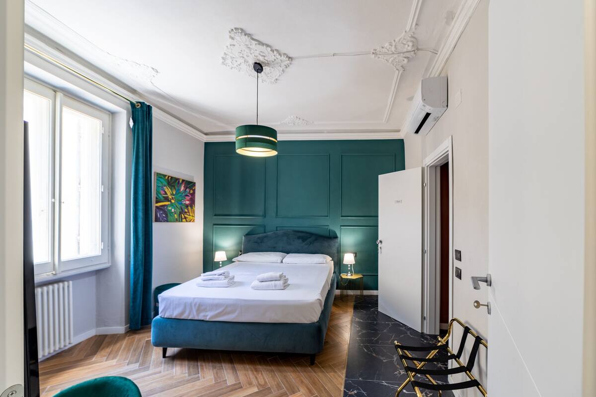 A bedroom with a bed, two bedside tables with lamps, a window with curtains, and a radiator.