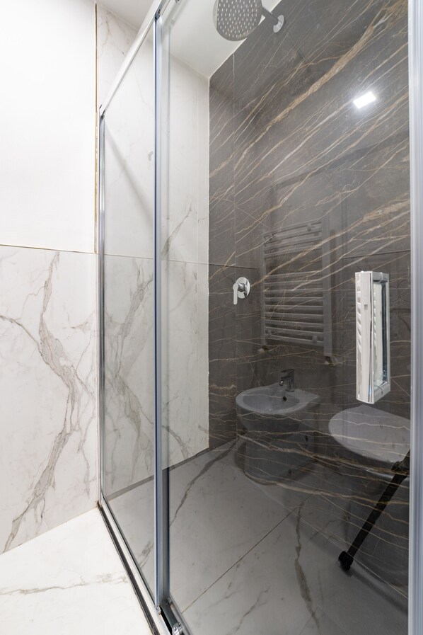 Un baño moderno con cabina de ducha de vidrio, azulejos de mármol, un lavamanos y un perchero.