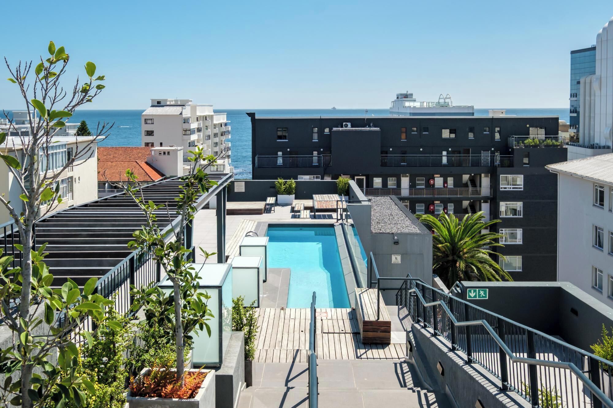 A rooftop pool with a view of the sea, surrounded by modern buildings.
