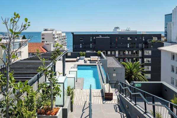 A rooftop pool with a view of the sea, surrounded by modern buildings.