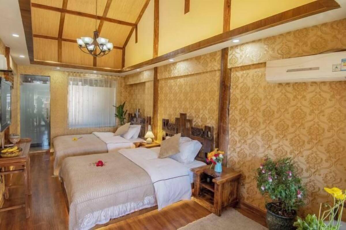 A hotel room with two beds, wooden beams, a chandelier, a potted plant, and an air conditioning unit.