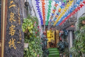 A narrow alleyway with a variety of plants and colorful pinwheels.