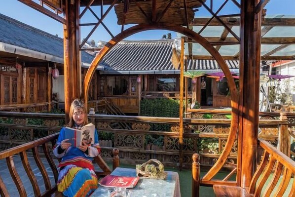 A traditional wooden structure with a covered seating area, a table with a book and a red object, and a view of a building with a tiled roof.