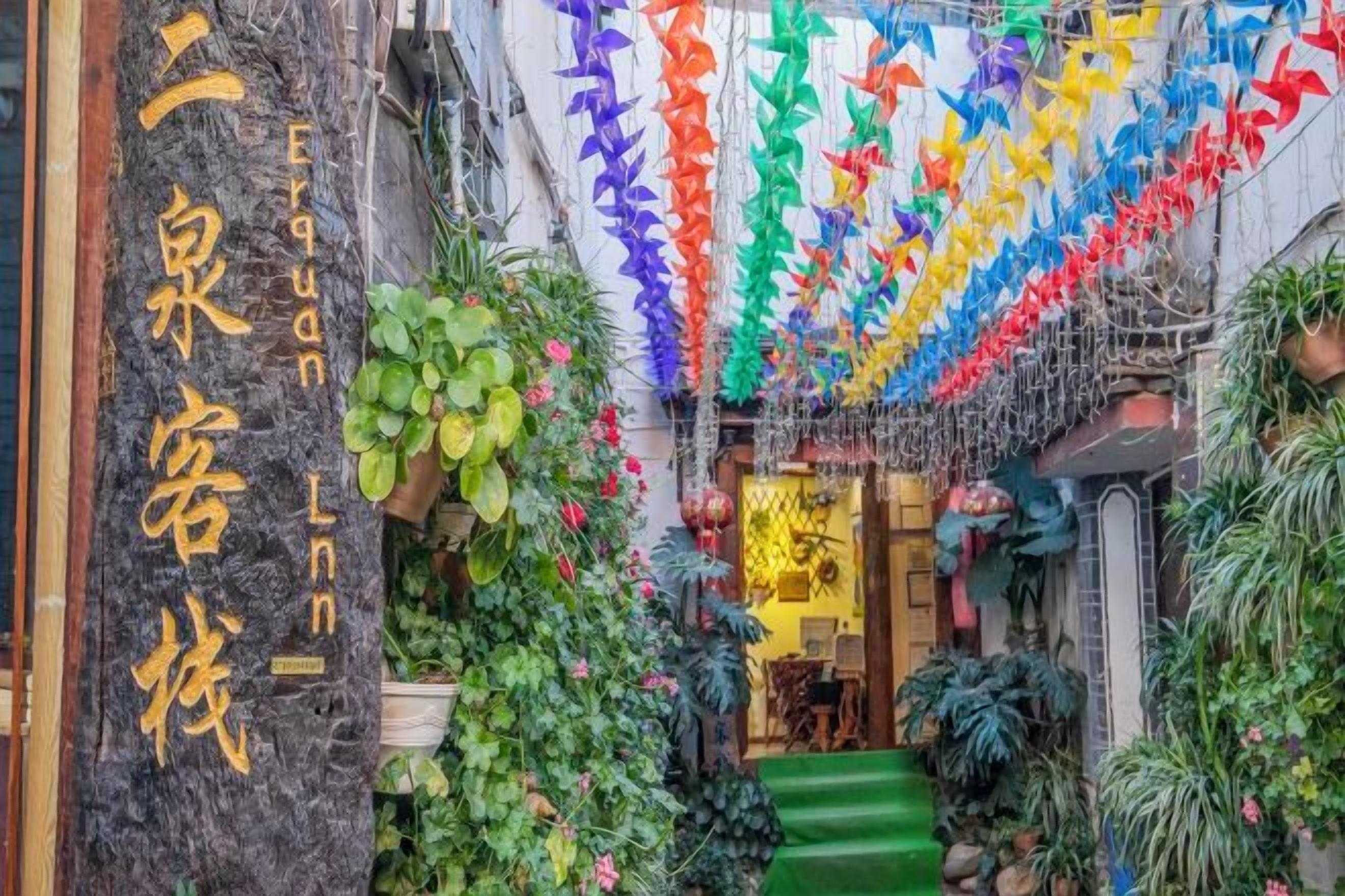 Un carrer estret amb una escala que condueix a una porta, envoltat de verdura exuberant i elements decoratius penjants.