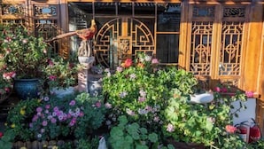 A traditional Chinese garden with a wooden gate, potted plants, and a statue.
