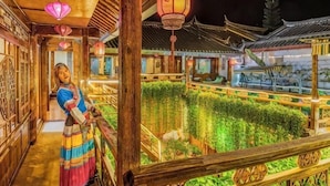 A traditional Chinese courtyard with wooden architecture, a person in traditional attire, and a well-maintained garden.