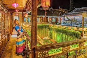 A traditional Chinese courtyard with wooden architecture, a person in traditional attire, and a well-maintained garden. - Erquan Inn (Lijiang)