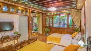 A room with two beds, a TV, wooden furniture, and a large window with a view.