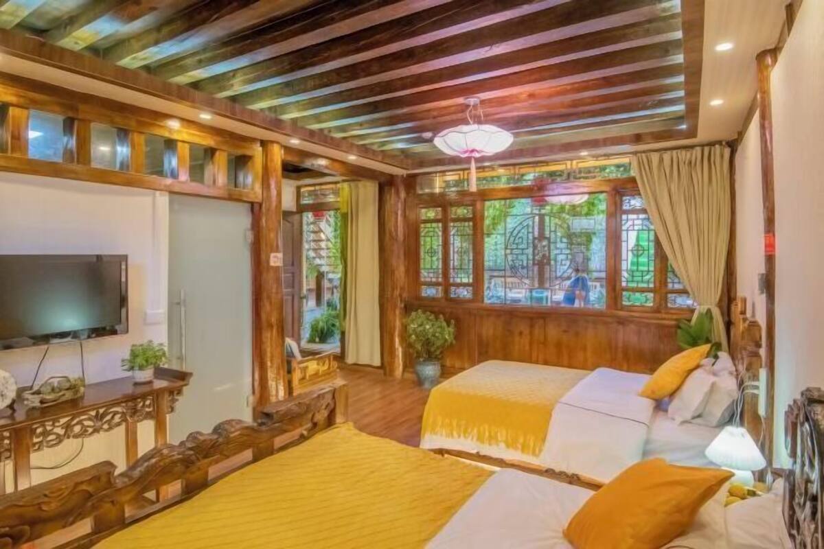 A room with two beds, a TV, wooden furniture, and a large window with a view.