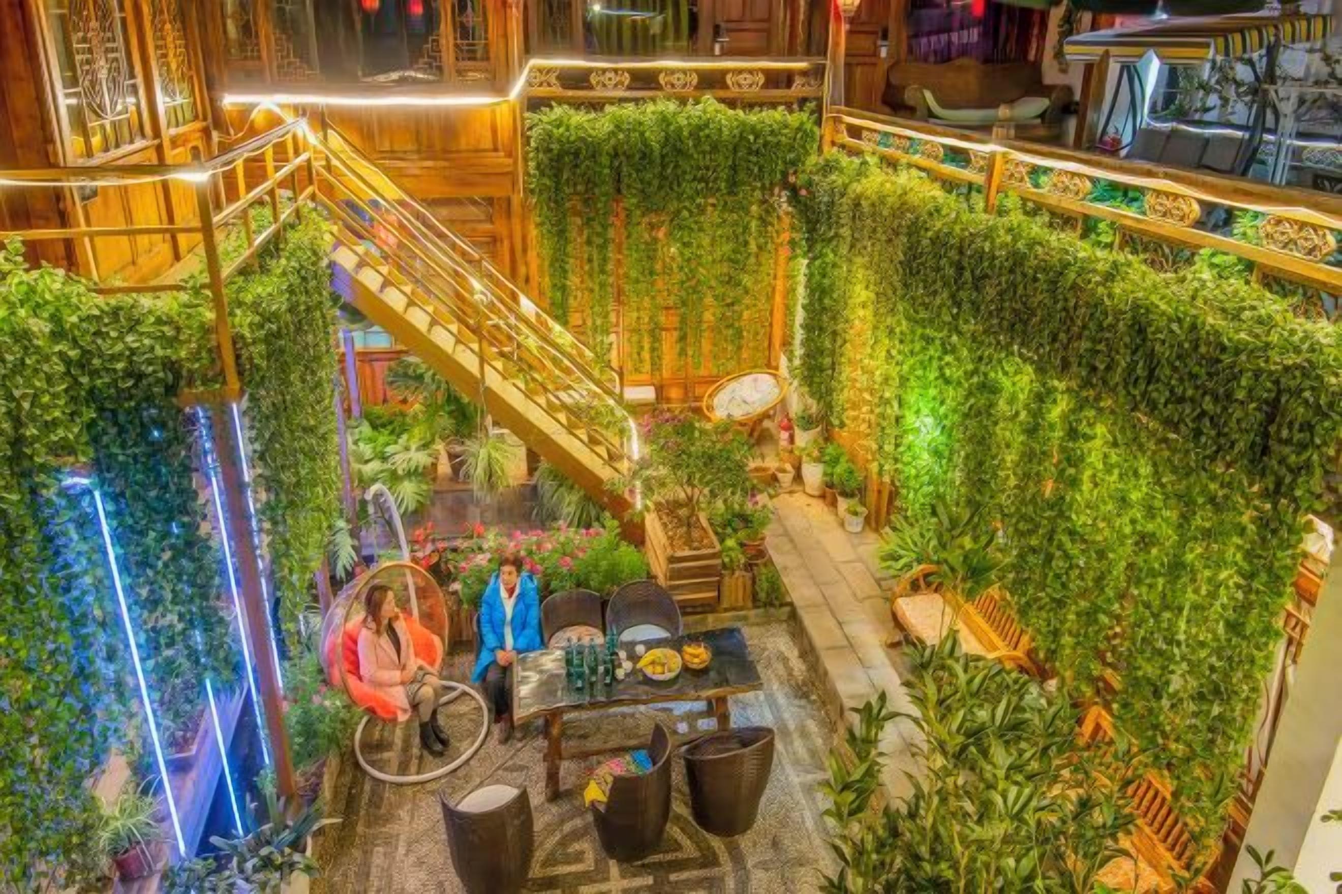A hotel lobby with a central staircase, lush vertical greenery, and a seating area with tables and chairs.