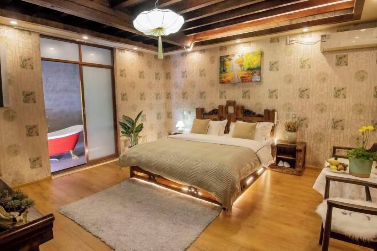 A bedroom with a large bed, wooden headboard, a nightstand, a potted plant, and a painting on the wall.