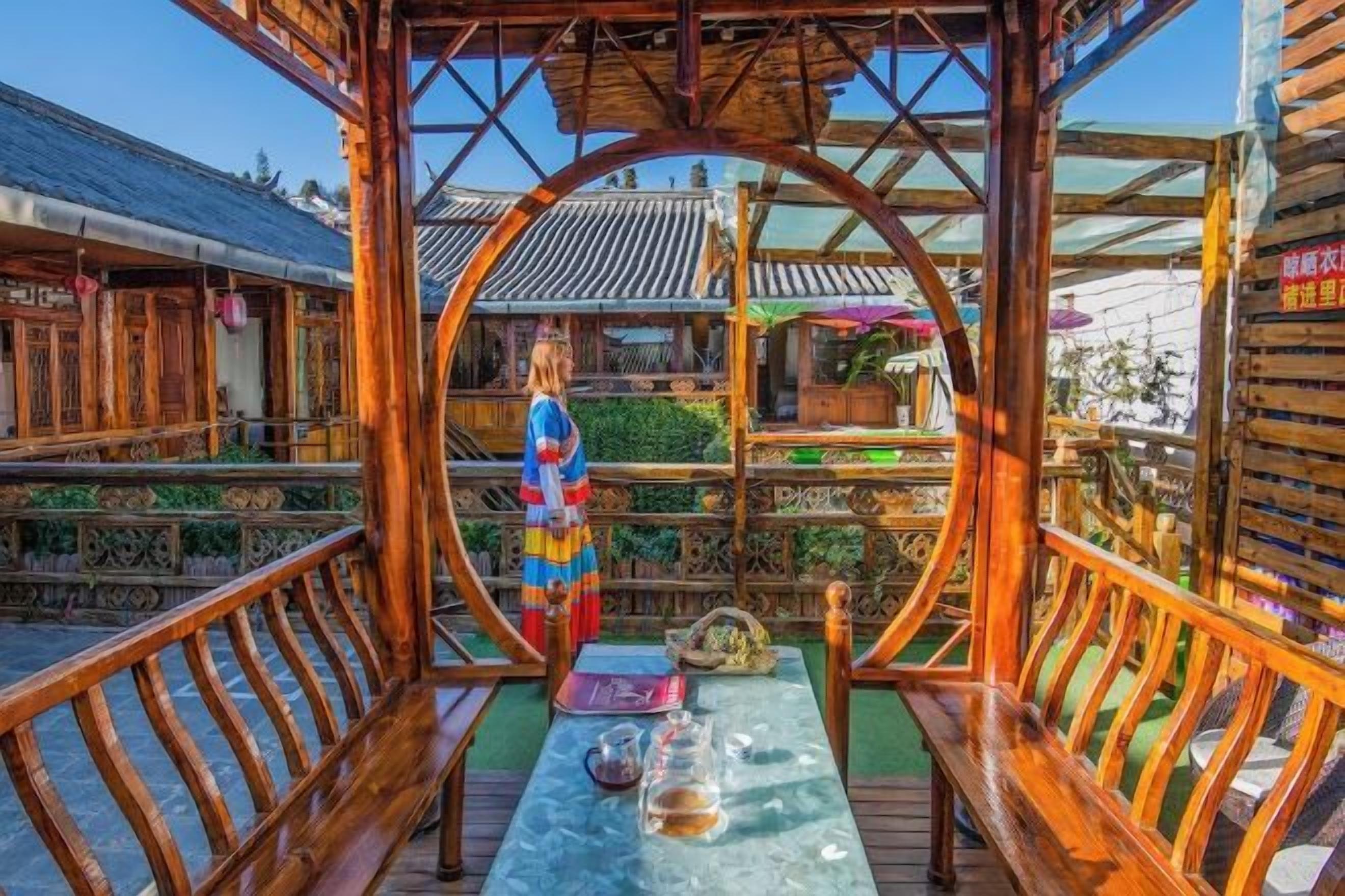 Eine traditionelle Holzhütte mit Tisch, Bänken, einer Zierfigur und Blick auf ein Gebäude mit Ziegeldach.