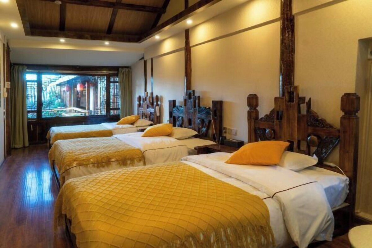 Ein Hotelzimmer mit drei Betten, Holzkopfteilen und Blick auf ein traditionelles Gebäude.
