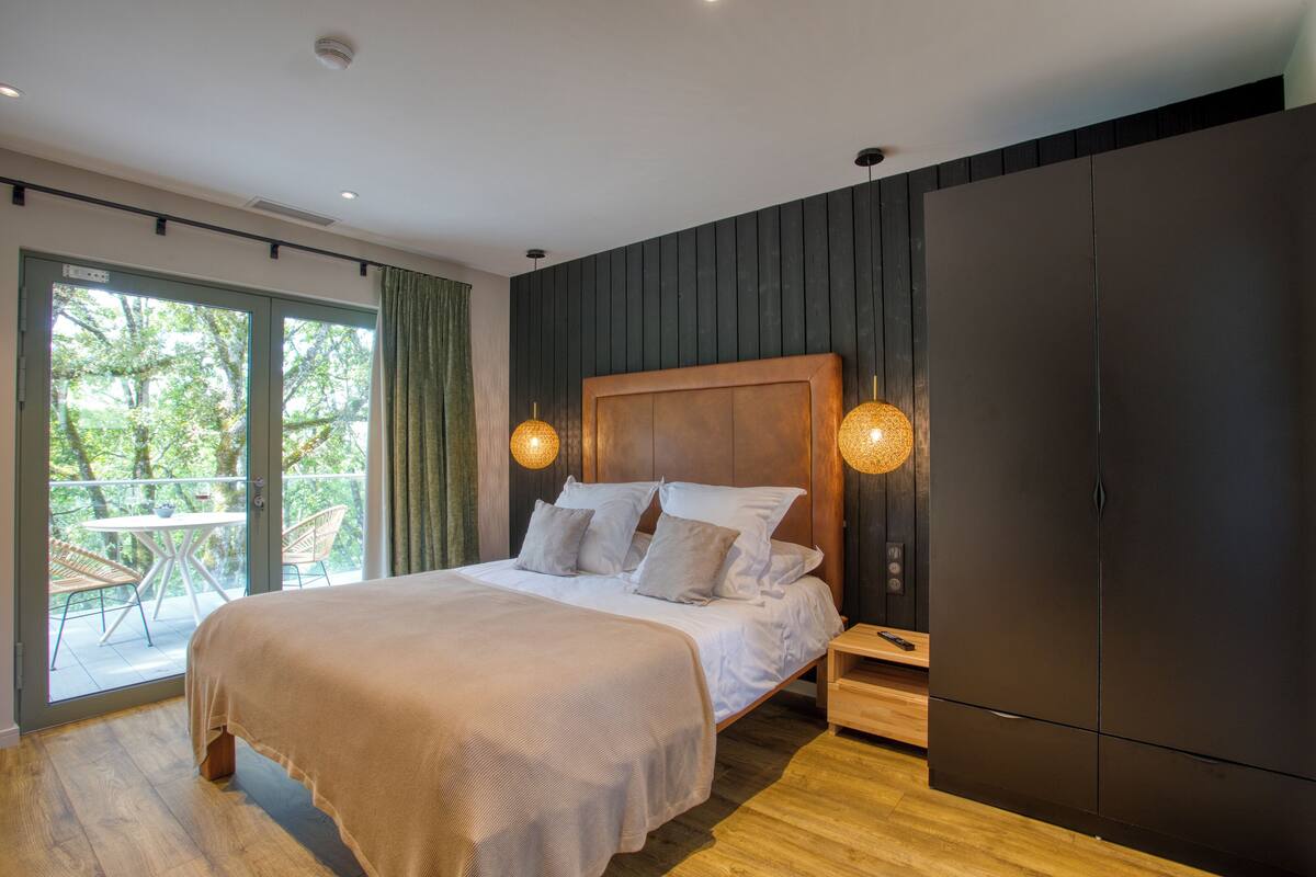 A modern bedroom with a large bed, wooden headboard, and a sliding door leading to a balcony.