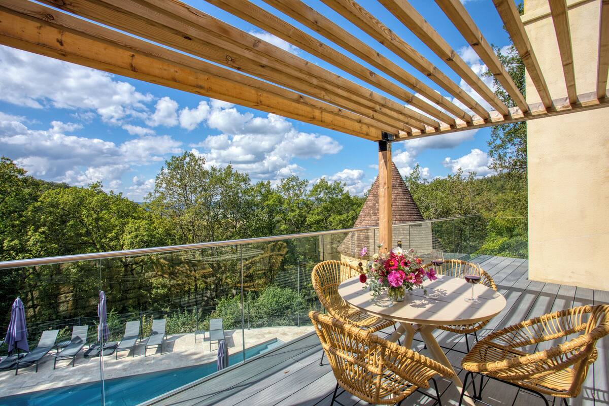 A wooden deck with a pool, wicker chairs, and a table with a vase of flowers.