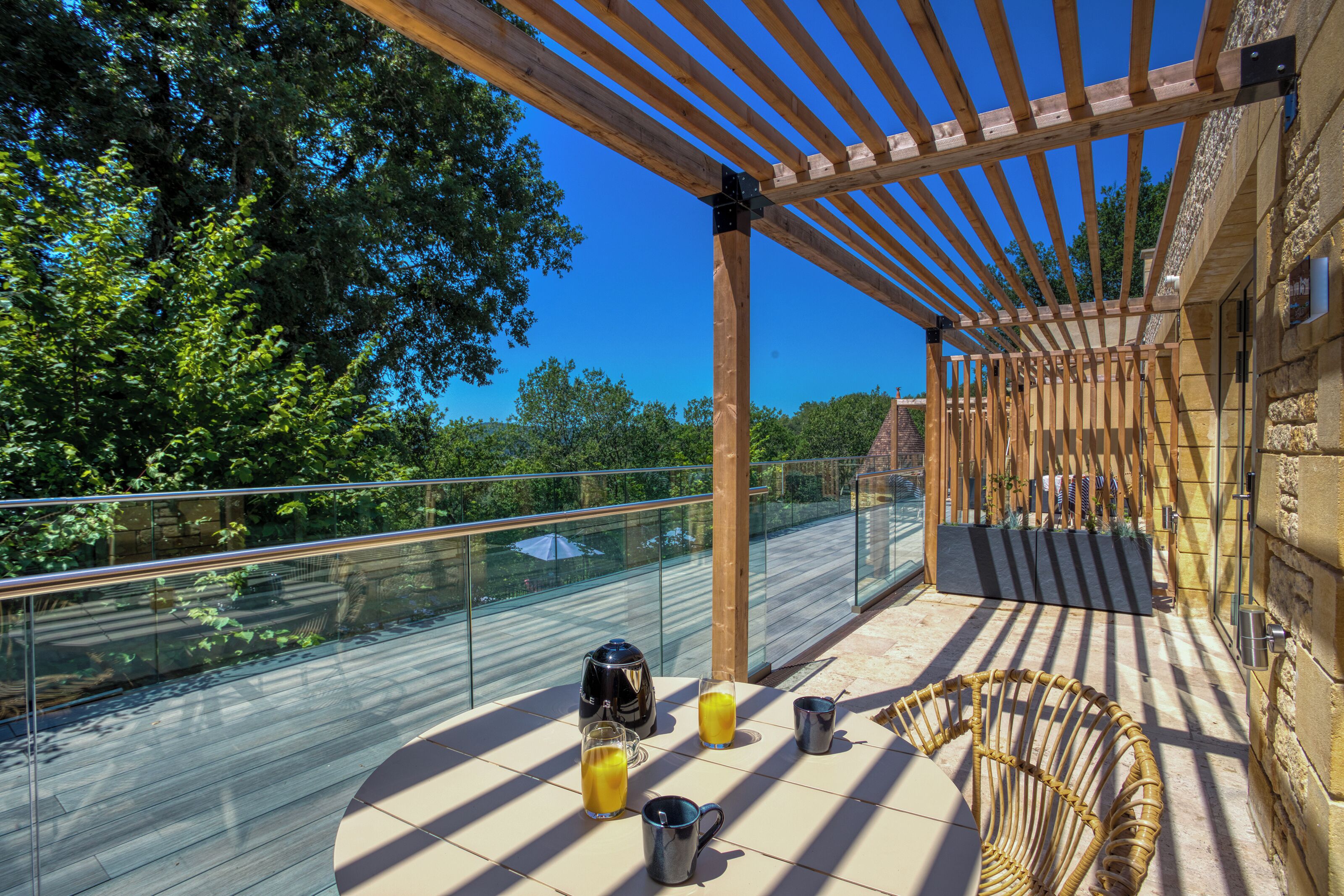 A covered outdoor area with a glass railing, wooden pergola, and a wicker chair.