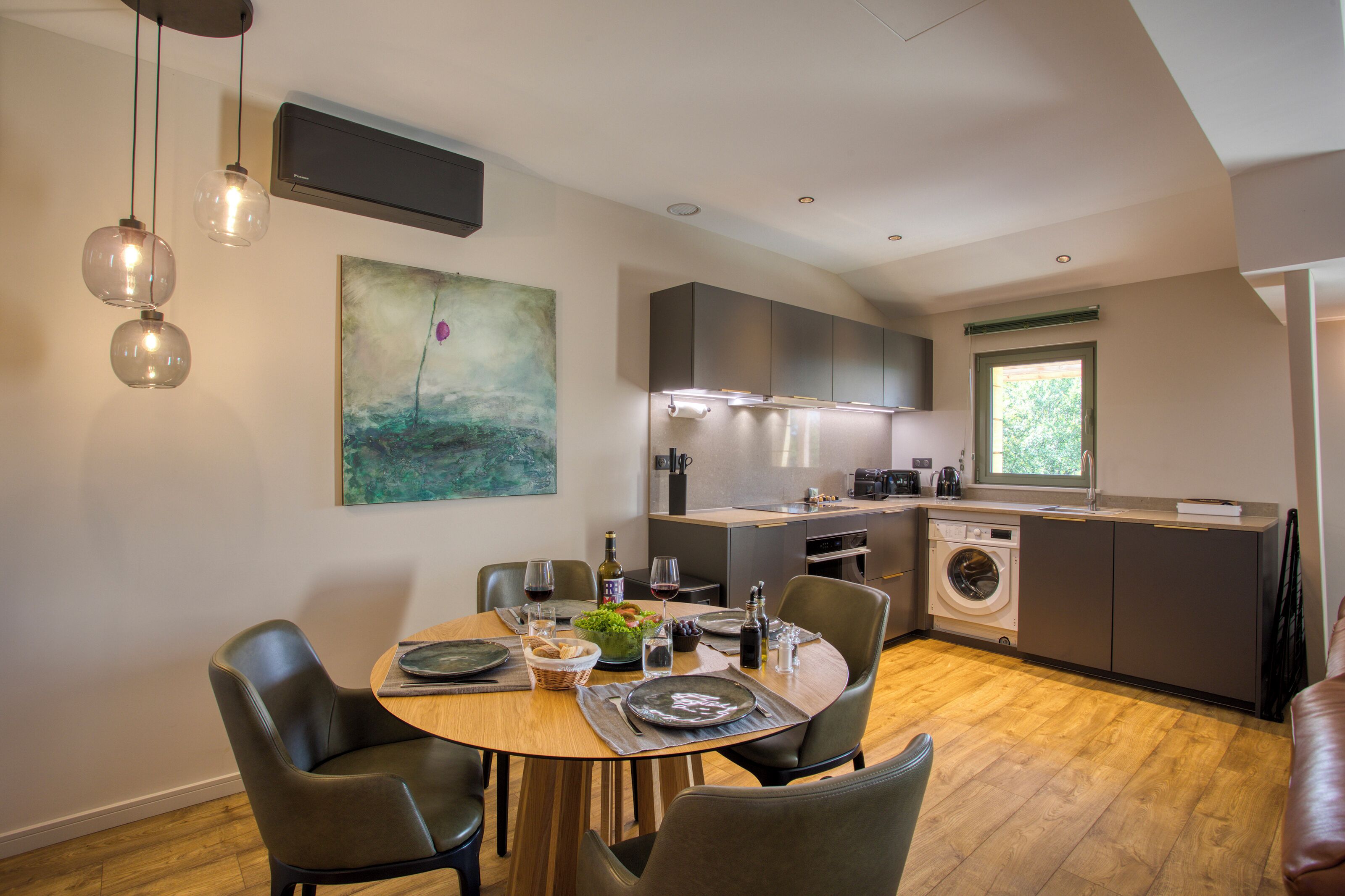 A modern kitchen with a dining area, including a table set for two, a washing machine, and a window with a view.