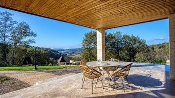 Un patio al aire libre con techo de madera, una mesa redonda con sillas y vista al campo.