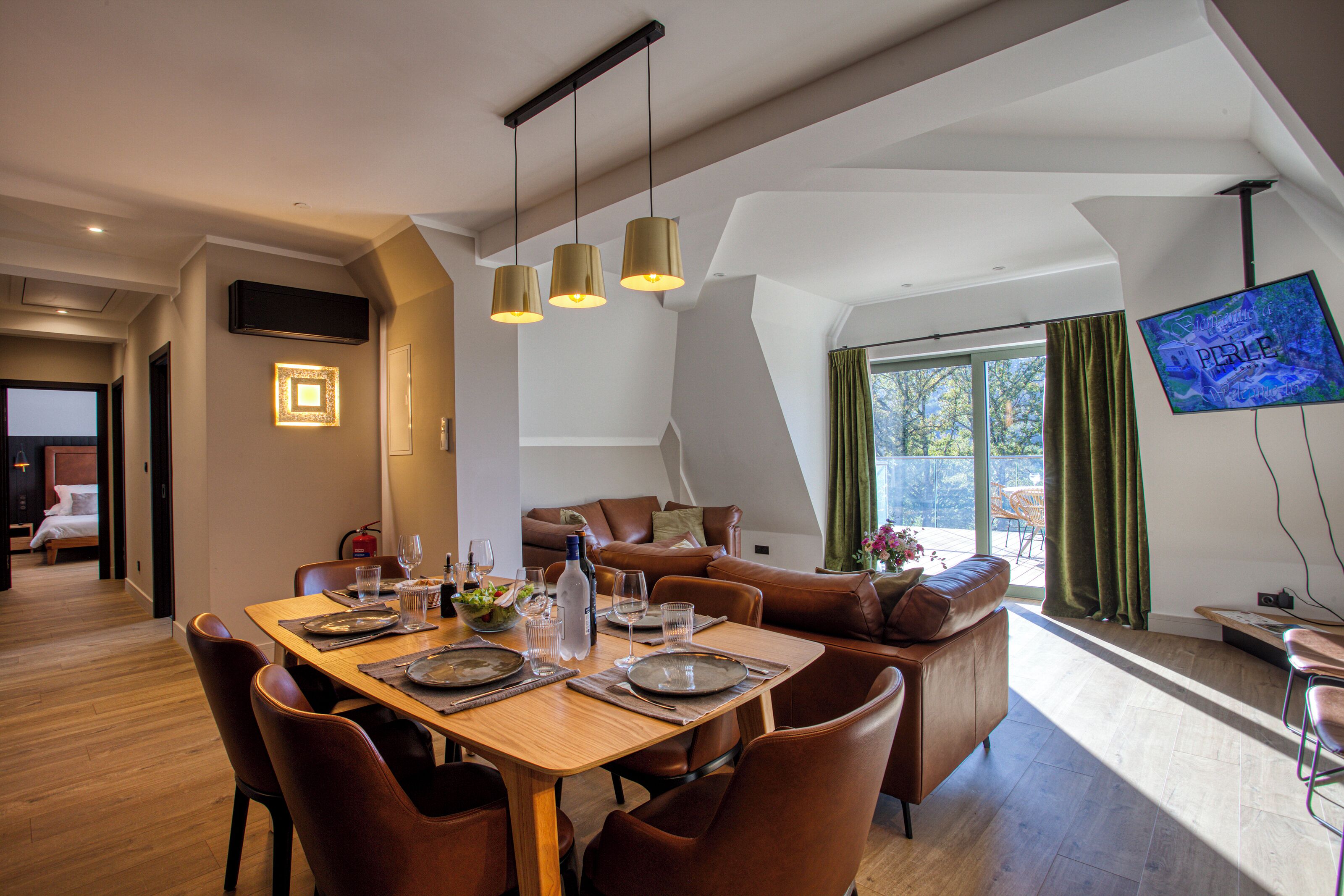 Un comedor moderno con una mesa de madera dispuesta para cuatro, un sofá y un televisor montado en la pared.