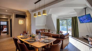 Un comedor moderno con una mesa de madera dispuesta para cuatro, un sofá y un televisor montado en la pared.