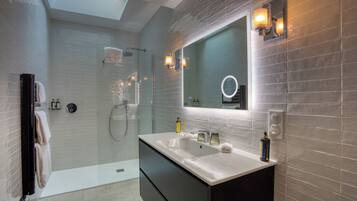 Un baño moderno con ducha envuelta en vidrio, un espejo grande con apliques de pared y un mueble de tocador con lavabo y cajones para guardar.