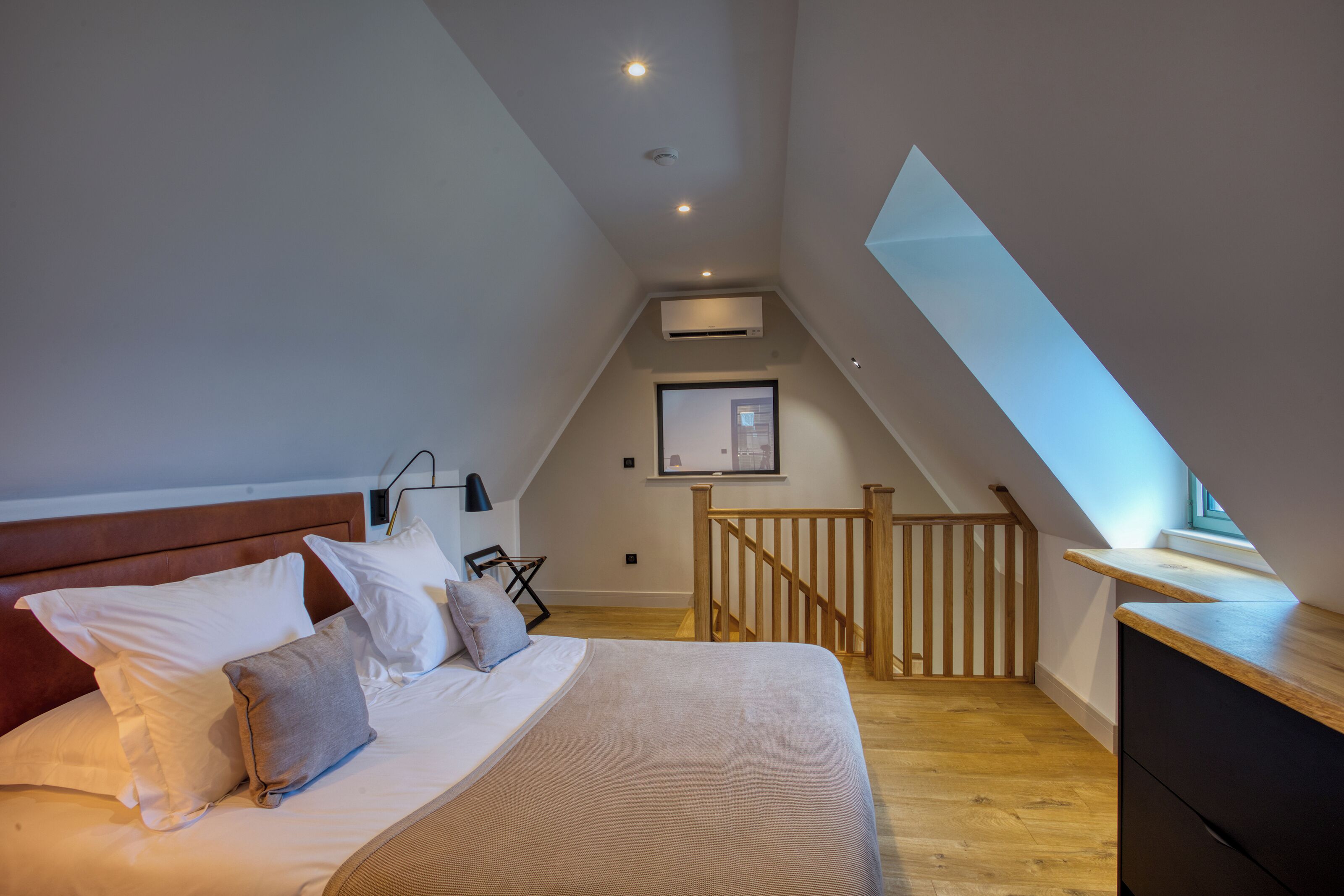 A bedroom with a bed, pillows, a desk, and a wooden railing.