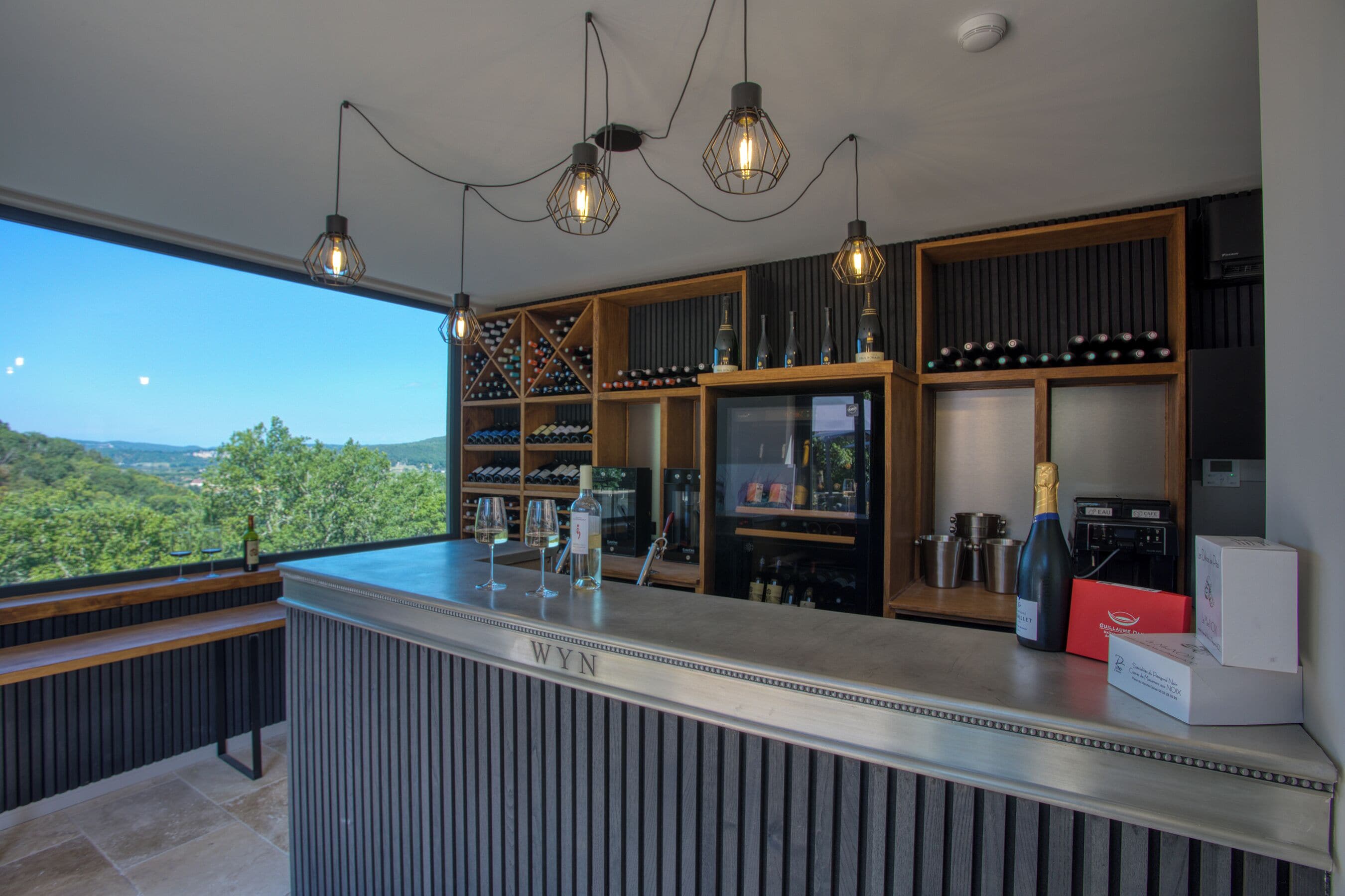Een moderne bar met uitzicht op het omliggende landschap, wijnglazen en cocktailglazen, en een bar met de naam 'WYN'.