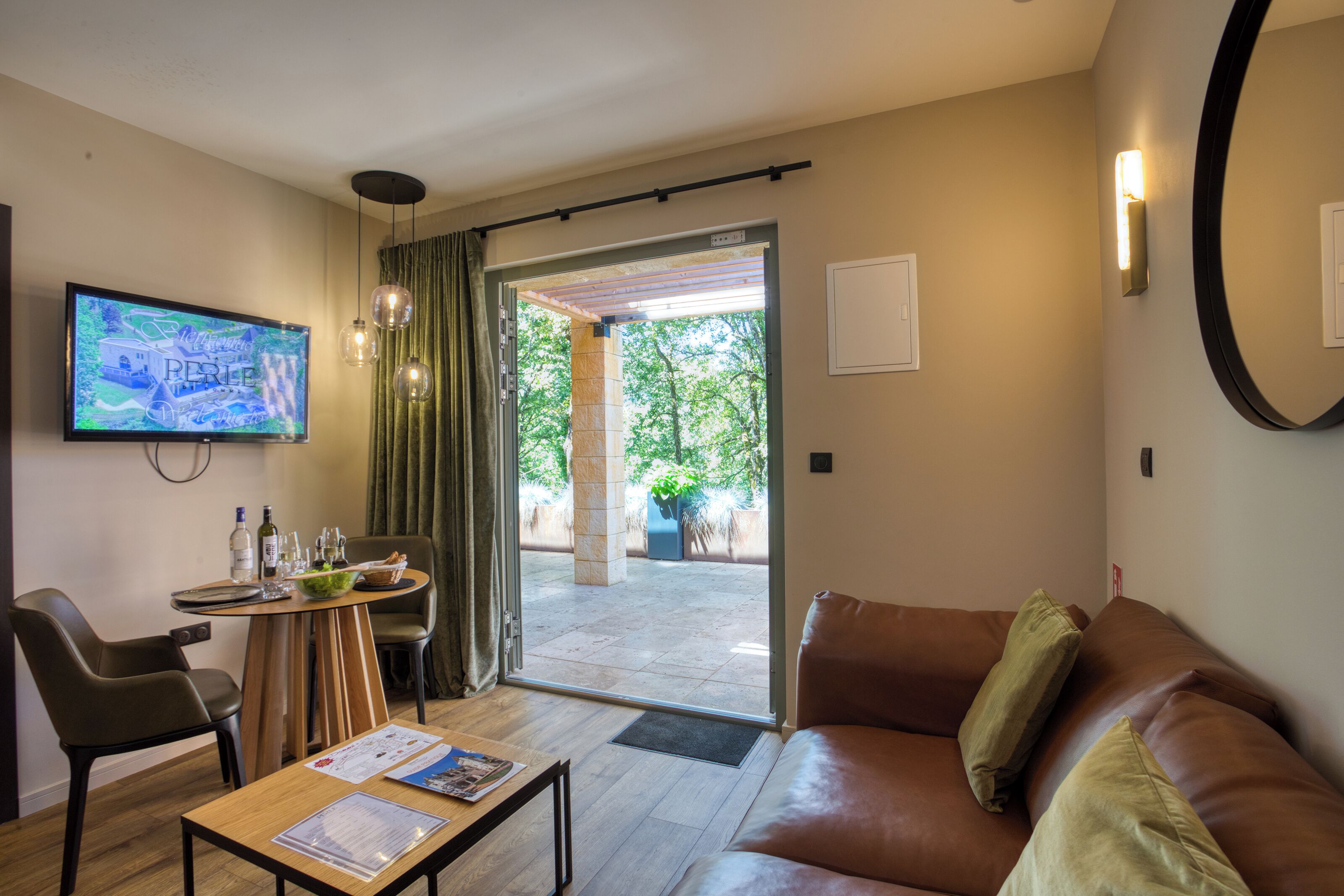 Une chambre d’hôtel moderne équipée d’un canapé, d’une table à manger et d’un téléviseur diffusant une émission.