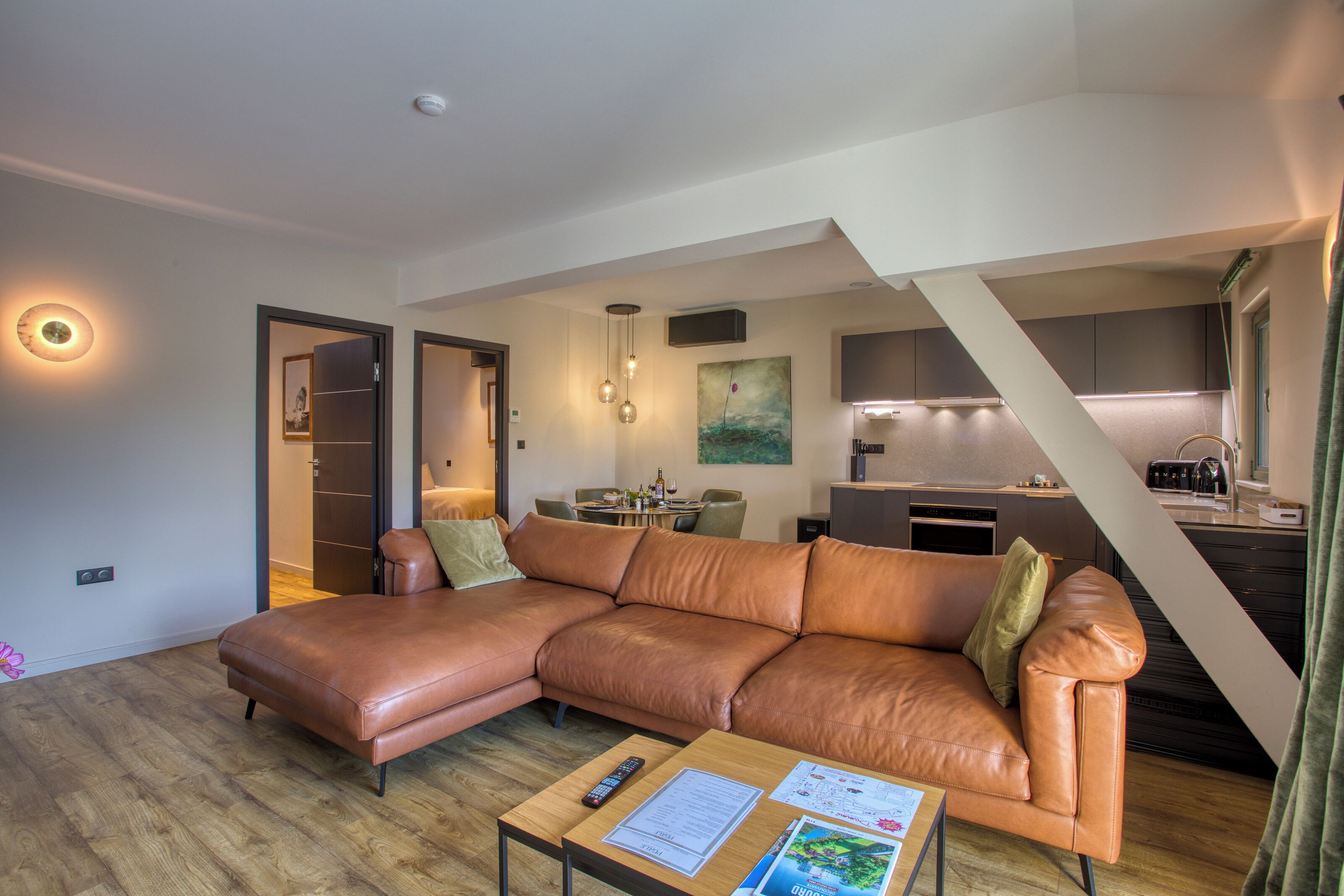 A modern living room with a brown leather sofa, a wooden coffee table, and a dining area with a table and chairs.