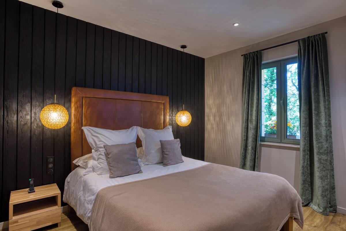 A bedroom with a wooden headboard, two bedside lamps, a nightstand, and a window with curtains.