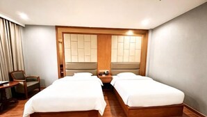 A hotel room with two single beds, a wooden headboard, a nightstand, a chair, and a desk.